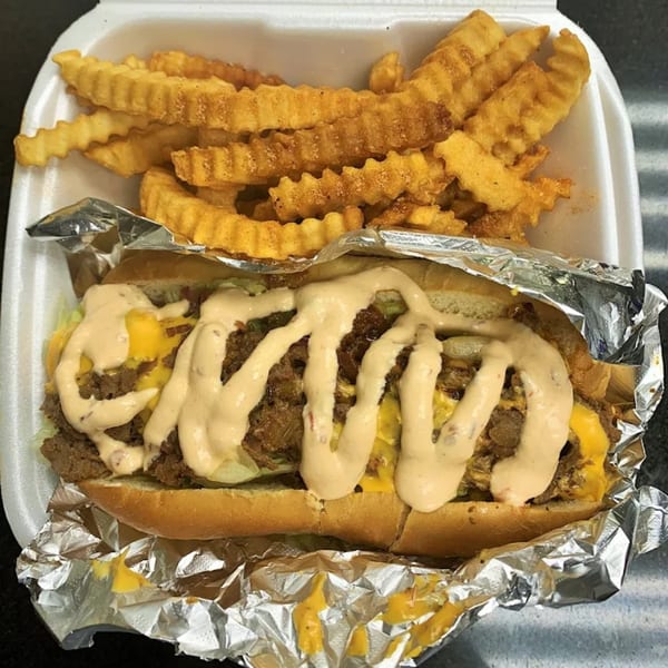 Arhiboo Shawarma's cheesesteak with sauce and crinkle-cut fries in a white takeout container.